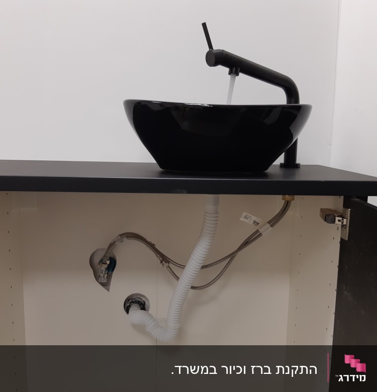 כיור שחור עם ברז, צינורות מתחת לארון